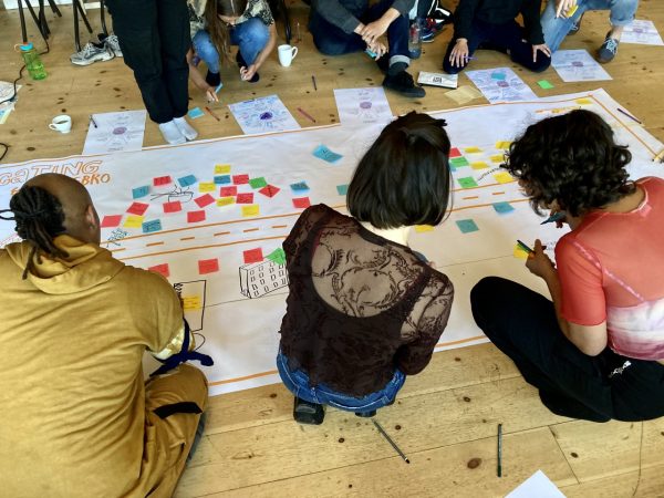 Three people are photographed from behind while sitting on the floor working on a big map of Nørrebro full of post-it notes.